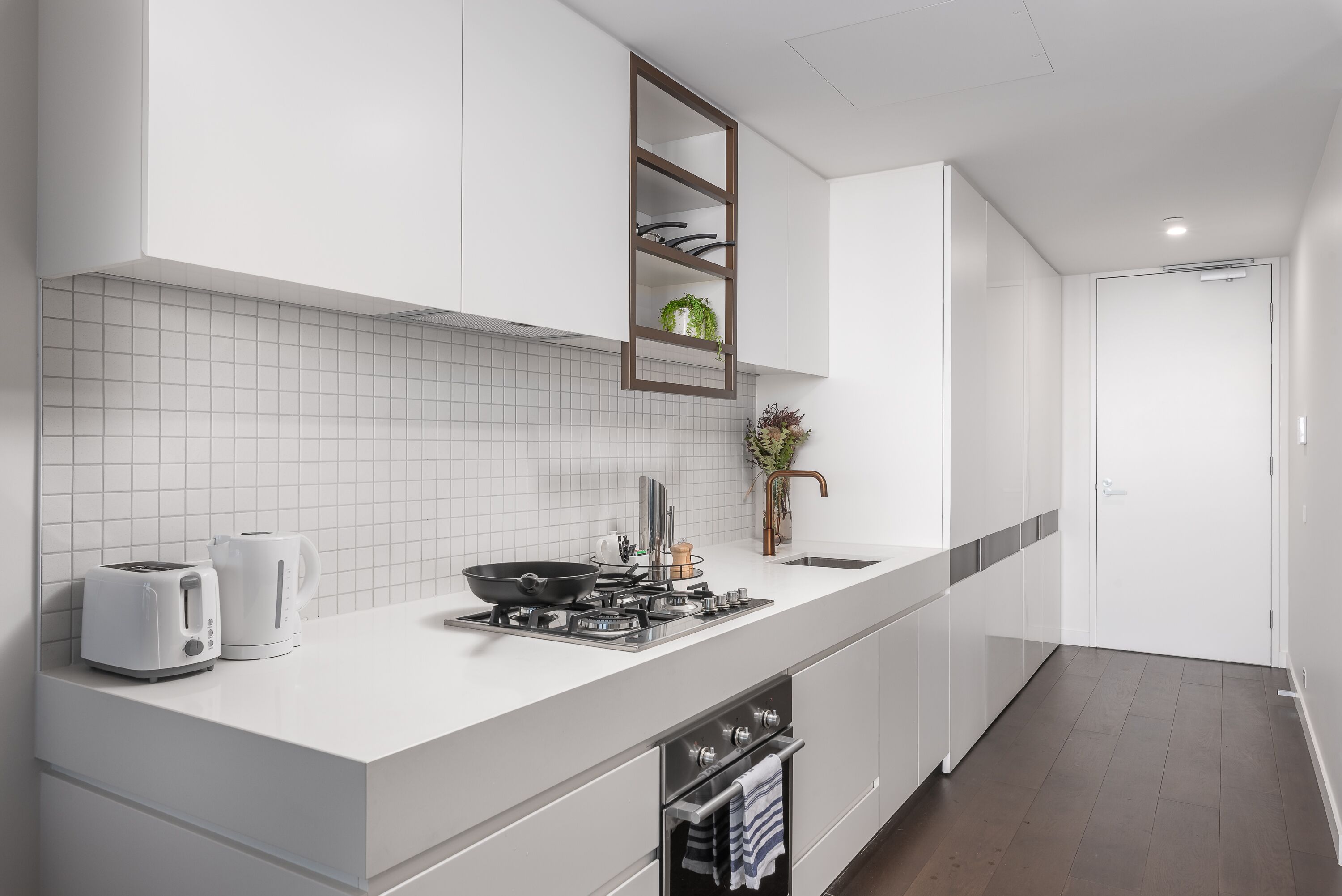 A modern kitchen with white cabinetry, a tiled backsplash, a built-in stove, and a countertop with a kettle and toaster.