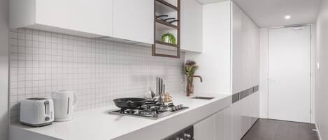 A modern kitchen with white cabinetry, a tiled backsplash, a built-in stove, and a countertop with a kettle and toaster.