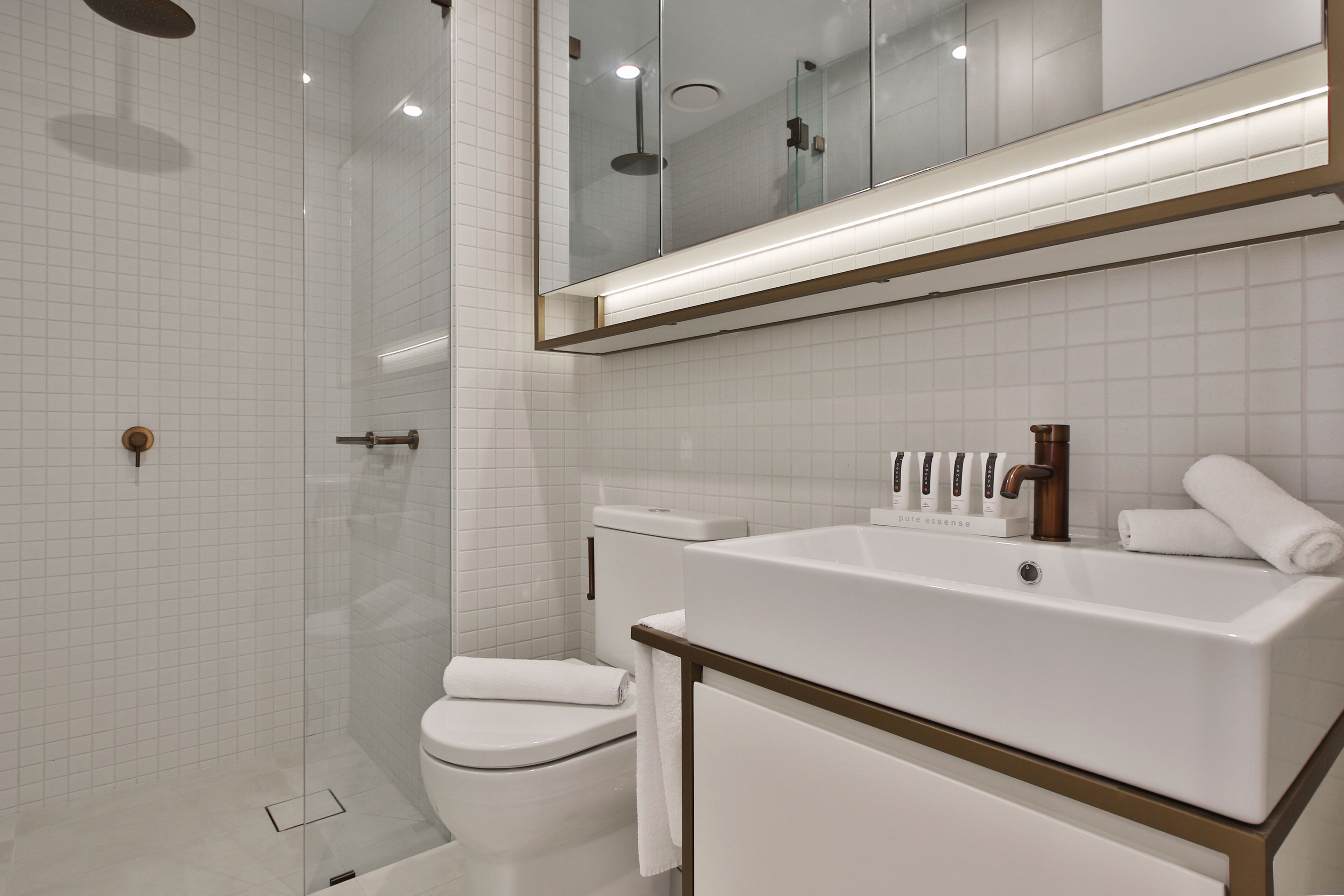 Un baño moderno con cabina de ducha de vidrio, inodoro blanco, lavamanos grande con espejo y una toalla sobre el lavamanos.