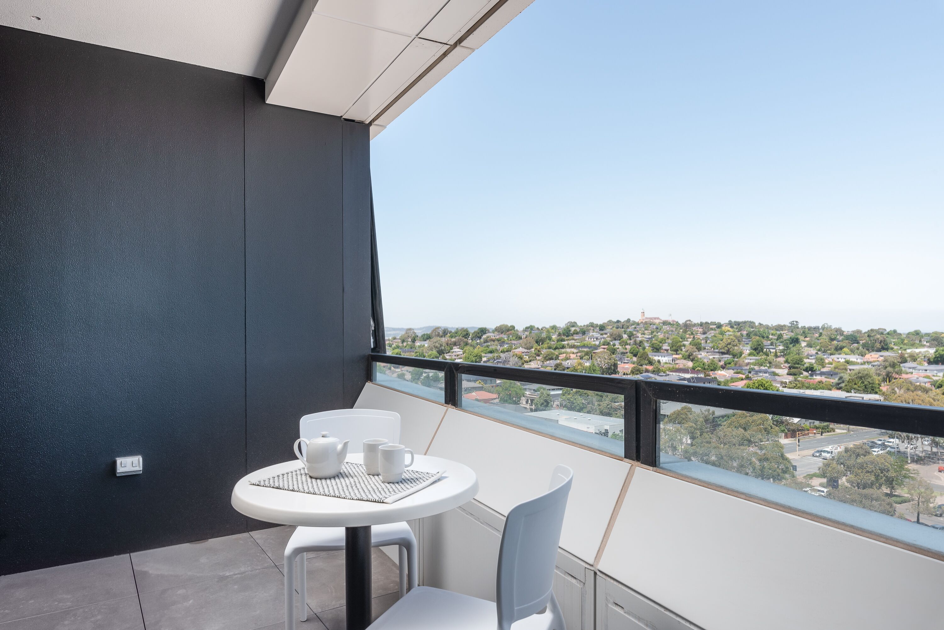A balcony with a table and chairs, a view of a residential area, and a power outlet on the wall.