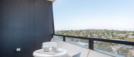 A balcony with a table and chairs, a view of a residential area, and a power outlet on the wall.