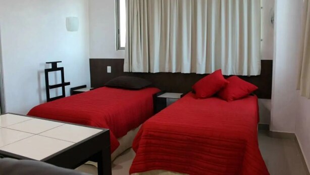 Habitación de hotel con dos camas individuales, una mesita y una ventana con cortinas.