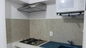 Cocina compacta con estufa a gas, microondas y pileta azul.