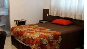 Habitación de hotel con cama, mesita de noche, ventana con cortinas y puerta.
