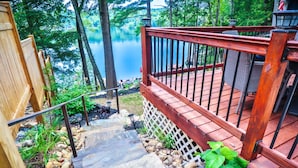 A wooden deck with a metal railing leading to a stone staircase surrounded by rocks and greenery. - SHORELINE CHATEAU-LAKEFRONT-LARGE DOCK-GAMEROOM- HOT TUB-WALK OUT DECK-LAKE VIEW (Fort Ann)