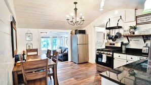 A kitchen with wooden flooring, a dining area with a table and chairs, a refrigerator, a stove, and a microwave. - SHORELINE CHATEAU-LAKEFRONT-LARGE DOCK-GAMEROOM- HOT TUB-WALK OUT DECK-LAKE VIEW (Fort Ann)