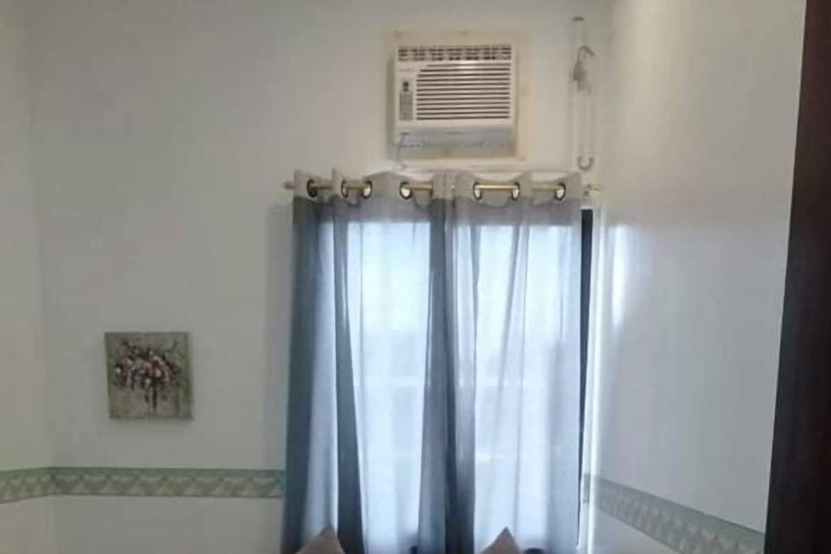 A hotel room with a bed, two pillows, a bedside table with a lamp, and a painting on the wall.