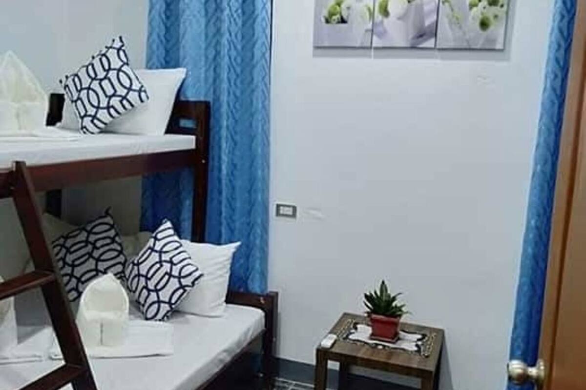 A small, well-lit room with a bunk bed, a small table with a plant, and a wall-mounted air conditioner.