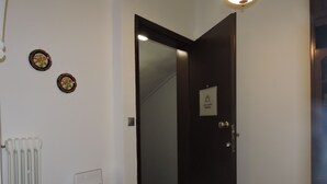 Een gang met een radiator, een bureau met een apparaat, en een deur met een bordje.