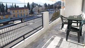 Een balkon met uitzicht op een straat en gebouwen, een tafel met stoelen en een metalen hekwerk.
