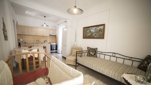 Een gezellige woonkamer met een bank, een klein bed, een stoel en een eethoek met een tafel en stoelen.