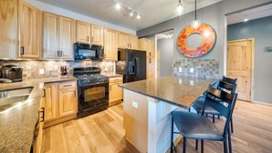 A modern kitchen with wooden cabinets, stainless steel appliances, a granite countertop, and a central island with bar stools. - Four-Season Winter Park Condo w/ Pool Access! (Winter Park)