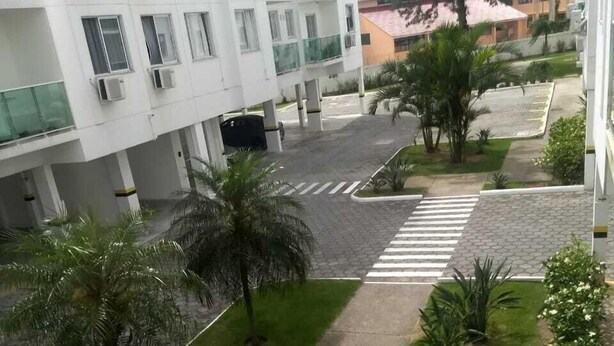 A courtyard with a crosswalk, palm trees, and a building with multiple floors and balconies. - Apto 2 Quartos na Praia da Cachoeira (Florianópolis)
