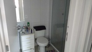 A small bathroom with a toilet, a sink, and a shower. - Apto 2 Quartos na Praia da Cachoeira (Florianópolis)