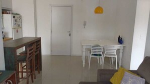 A living room with a dining area, a white door, and a yellow pendant light. - Apto 2 Quartos na Praia da Cachoeira (Florianópolis)