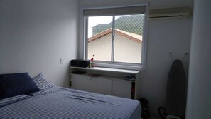Un dormitorio con cama, ventana, escritorio y una tabla de surf.