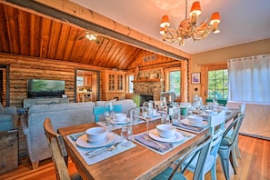 Acogedor interior de cabaña de madera con comedor listo para una comida, sala de estar con chimenea y televisor.