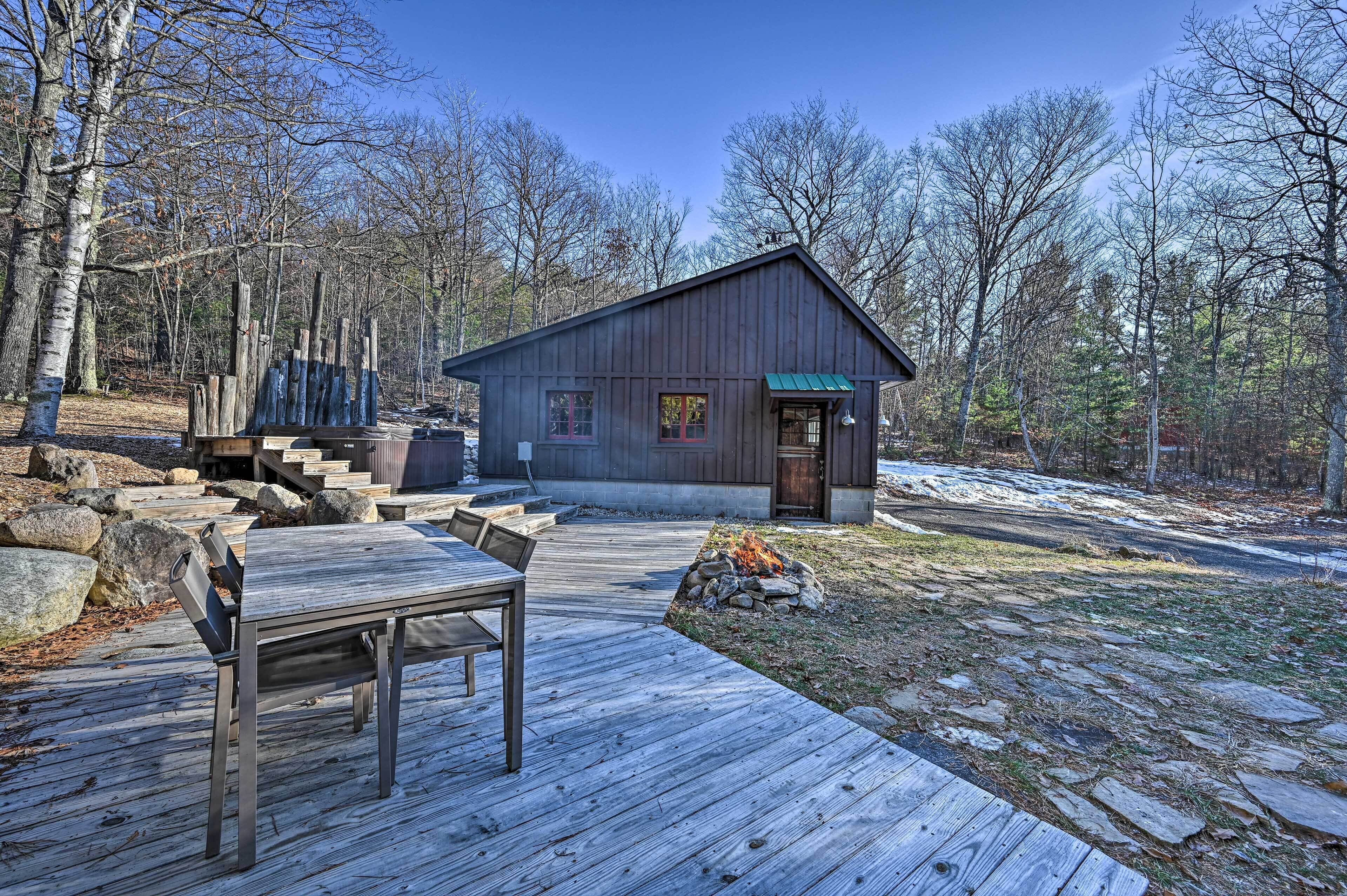 A cabin with a wooden deck, a fire pit, and a stone pathway leading to the entrance.