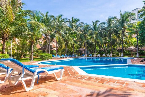 A swimming pool with lounge chairs and palm trees. - Familly Condo Beach w/ Free access 2 the Beach (Cancún)