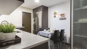 Eine moderne Küche mit Einbauofen, Mikrowelle und Kühlschrank. Es gibt eine Essecke mit Tisch und Stühlen sowie eine Topfpflanze auf der Arbeitsplatte.