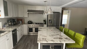 A modern kitchen with white cabinets, stainless steel appliances, a marble island, and a colorful rug. - Bayside Sunsets (Key Largo)