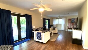 A spacious living room with hardwood flooring, a ceiling fan, a sofa, a coffee table, and a television. - Bayside Sunsets (Key Largo)