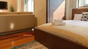 A hotel room with a bed, a sofa, a TV, and a window with curtains.