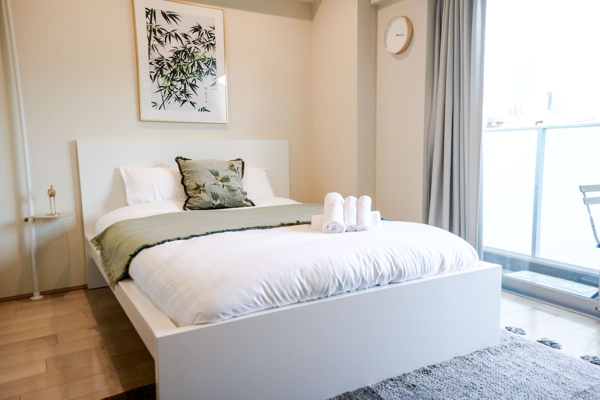 A modern bedroom with a large bed, a wall-mounted clock, and a window with curtains.