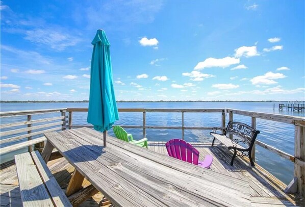 A wooden deck with a bench and chairs, overlooking a body of water.