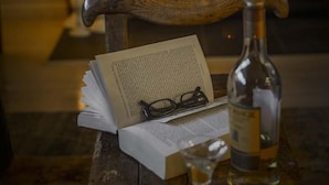 Een knus leeshoekje met een open haard, een houten stoel, een boek, brillen en een fles.