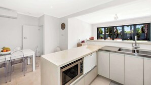 Una cocina moderna con encimera blanca, electrodomésticos de acero inoxidable y ventana con vista a palmeras.