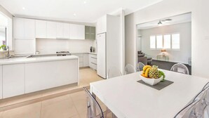 Una cocina moderna con armarios blancos, una isla central y un comedor con frutero.