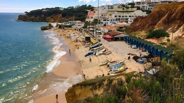 A coastal beach with a row of blue beach huts, a sandy shore, and buildings in the background.