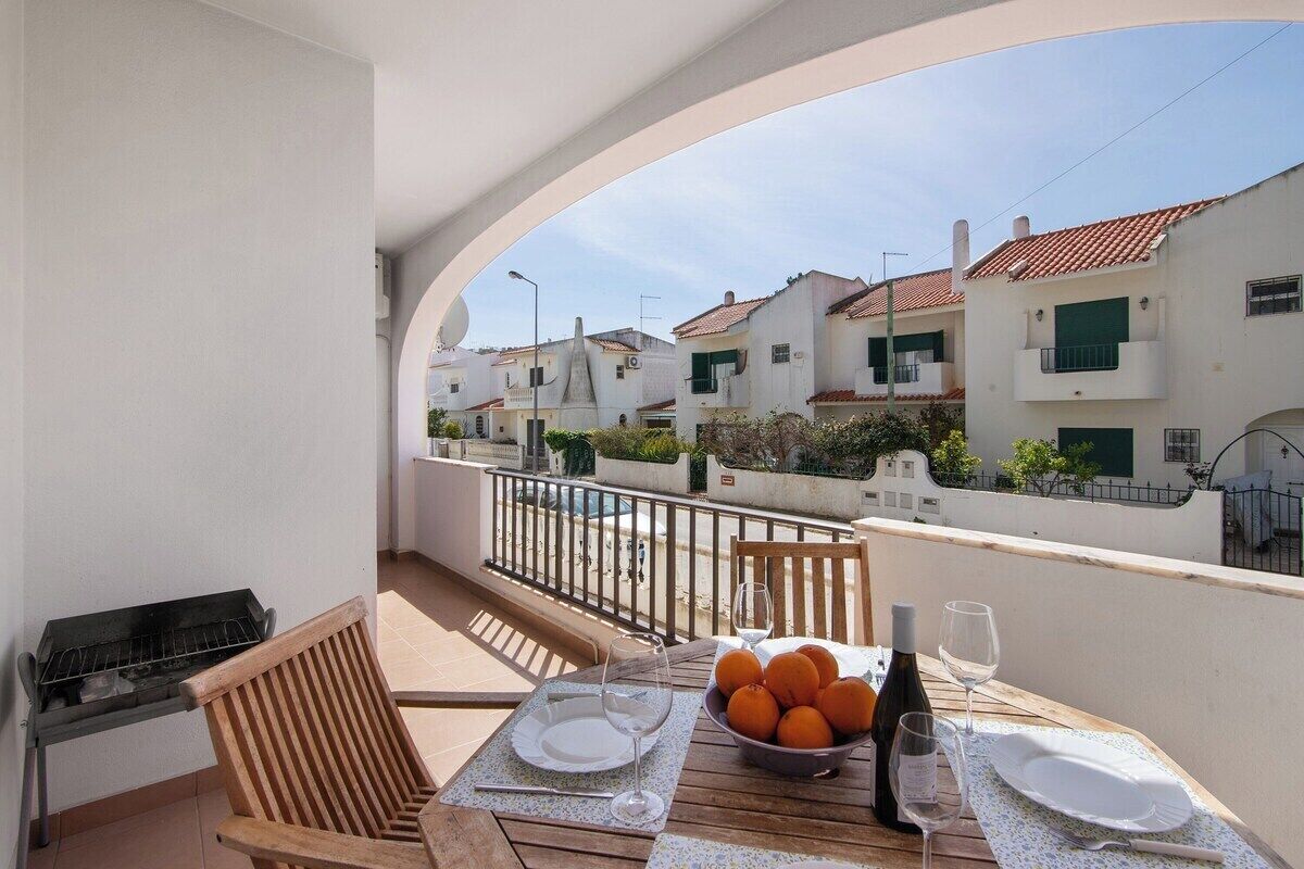 Een balkon met een tafel gedekt voor twee personen, een barbecue en uitzicht op witte gebouwen met rode daken.