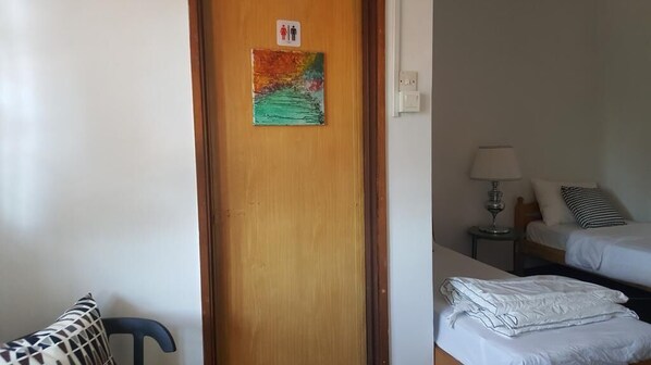 Une chambre d’hôtel avec une porte en bois, une œuvre d’art colorée, un lit avec une literie blanche, une table de chevet avec une lampe et une chaise avec un coussin à motifs.