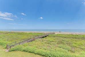 A wooden boardwalk leading to a beach with grassy terrain and a clear blue sky.