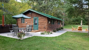 Une cabane en rondins avec une porte verte et un espace patio aménagé avec du mobilier d’extérieur.