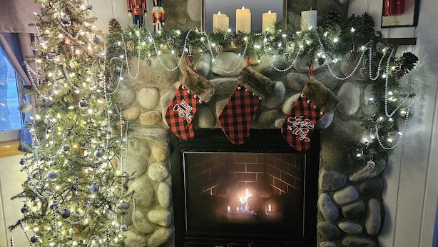 Une cheminée avec un manteau en pierre, un sapin de Noël décoré de guirlandes lumineuses, de chaussettes et de bougies.