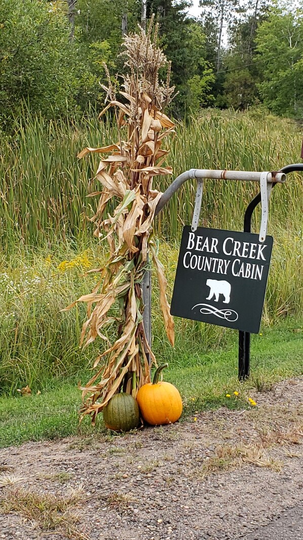 A sign for Bear Creek Country Cabin with a corn stalk and pumpkins.
