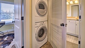 A laundry room with two front-loading washing machines, a window with blinds, and a bathroom with a vanity and mirror. - River Street Roost - 12 Miles to Sun Valley Resort (Hailey)