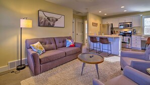 A living room with a sofa, a coffee table, and a lamp. There is a kitchen area with a refrigerator, microwave, and bar stools. - River Street Roost - 12 Miles to Sun Valley Resort (Hailey)