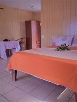 Una habitación con cama, un armario de madera, una mesita con mantel y una silla.