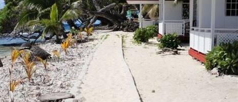 A beachfront property with a concrete walkway leading to a building with a red roof and white walls.