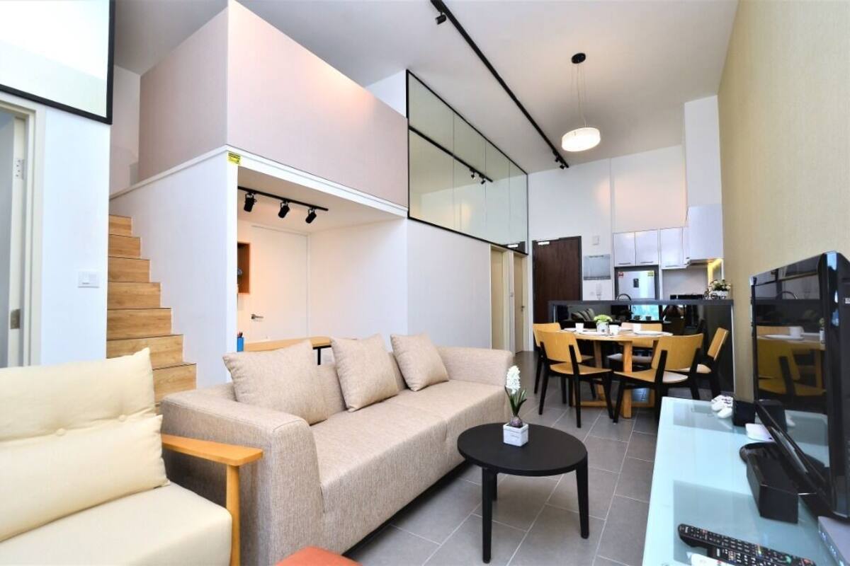 A modern living room with a sofa, coffee table, and dining area with chairs and a table. There is a kitchen in the background with cabinets and appliances.