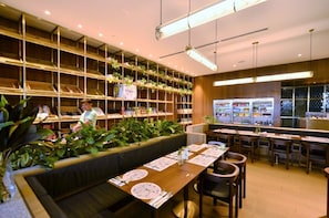 A modern restaurant with a long counter, shelves with plants, and a seating area with tables and chairs. - EST Link to LRT KL Sentral Bangsar (Kuala Lumpur)