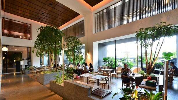 A spacious indoor area with multiple seating arrangements, including tables and chairs, surrounded by large potted plants and a central water feature. - EST Link to LRT KL Sentral Bangsar (Kuala Lumpur)