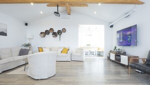 A spacious living room with a high ceiling, a white sofa set, a dining area, and a TV mounted on the wall.
