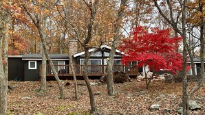 A cabin with a deck and a stone chimney, surrounded by trees with autumn leaves.