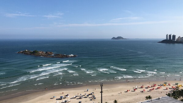 A beach with umbrellas and people, a rocky outcrop, and buildings in the distance. - HIGH STANDARD APARTMENT FACING THE SEA (Centro)