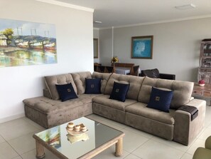 A living room with a beige sectional sofa, a glass coffee table, and a painting of boats on the wall. - HIGH STANDARD APARTMENT FACING THE SEA (Centro)